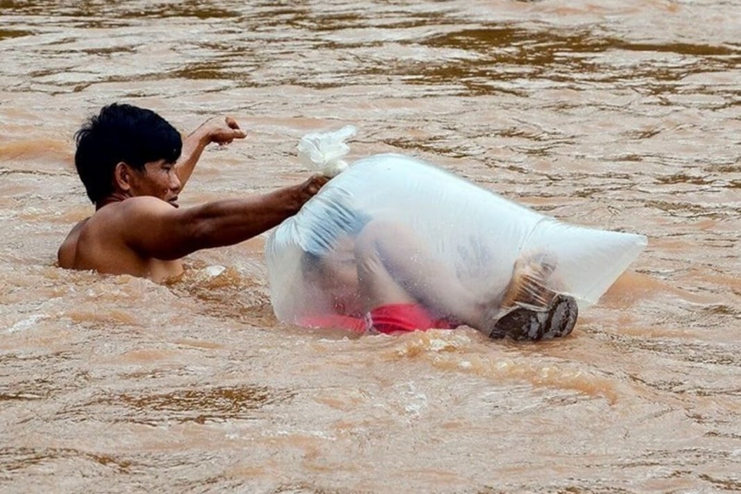 Para levar os filhos à escola, pais fazem a travessia do rio com as crianças dentro de sacos plásticos
