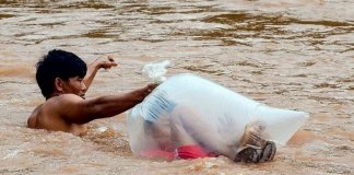 Para levar os filhos à escola, pais fazem a travessia do rio com as crianças dentro de sacos plásticos