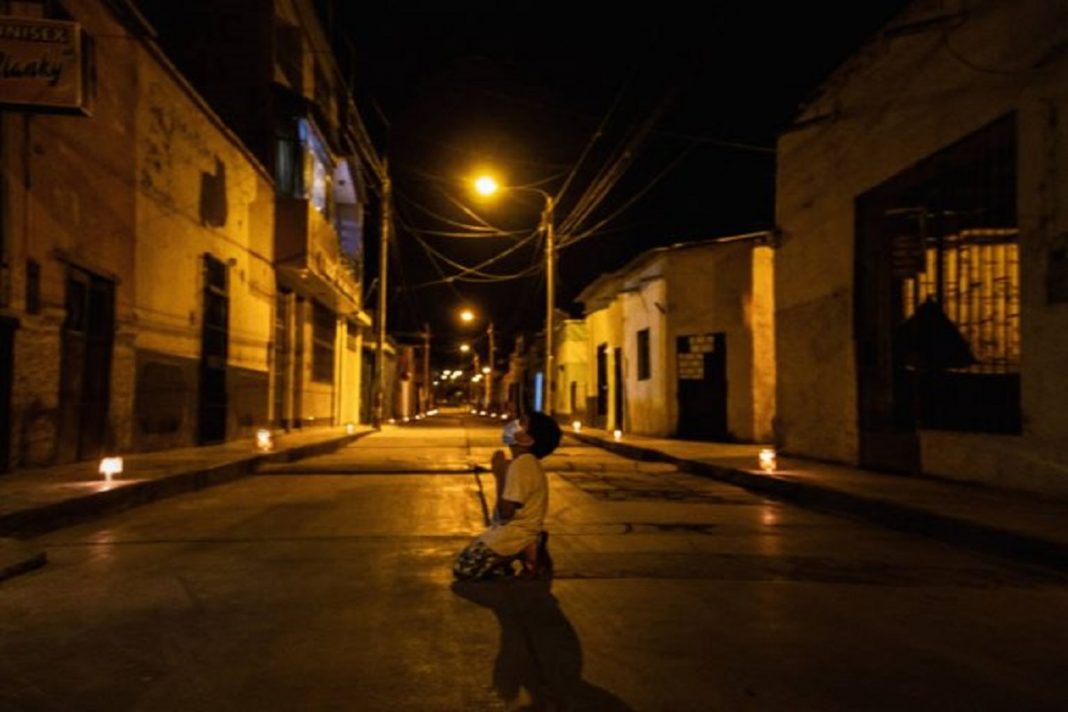 Criança reza de joelhos na rua pelo fim do coronavírus, durante toque de recolher no Peru