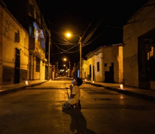 Criança reza de joelhos na rua pelo fim do coronavírus, durante toque de recolher no Peru