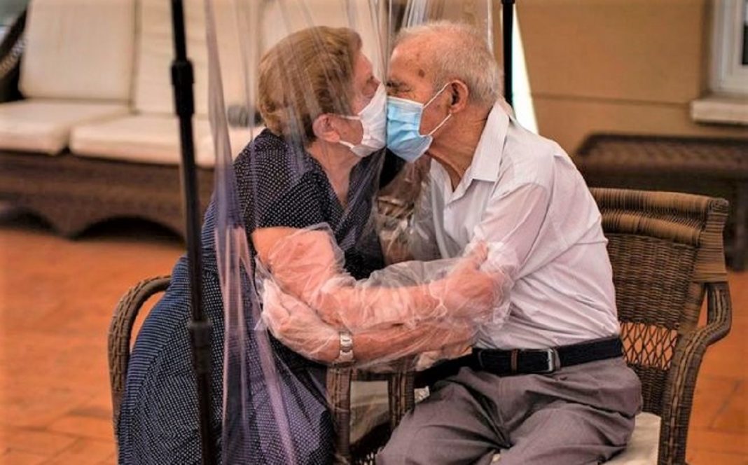 Casal de idosos se beijam na pandemia através de uma cortina plástica, provando que não há barreiras para o amor